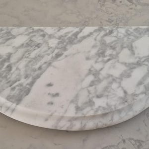 May include: A semi-circular marble board featuring a white base with prominent grey veining throughout the surface. The piece has a smooth, polished finish and a rounded edge that follows the curved perimeter of the stone slab design.