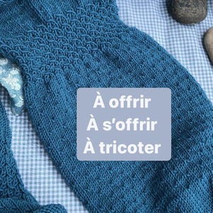 Peut inclure: Une écharpe tricotée bleu sarcelle avec un motif texturé. La laine est Lang Yarns Merino 120. Le texte sur l'étiquette indique "À offrir À s'offrir À tricoter".