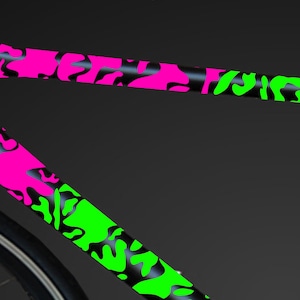 May include: A black bicycle frame with a pink and green camouflage pattern. The frame is made of carbon fiber and has a sleek, modern design.