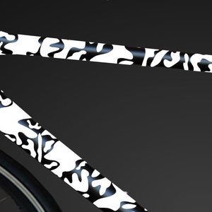 May include: Close-up of a black bicycle frame with a white camouflage pattern. The frame is made of carbon fibre and has a sleek, modern design.