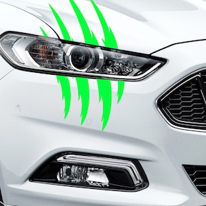 Op de afbeelding: Een witte auto met een groene klauwmarkering op de voorbumper. De auto heeft een zwarte grille en koplampen.