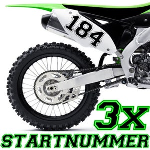 Könnte beinhalten: Ein grün-schwarzes Motocross-Motorrad mit einem weißen Nummernschild, auf dem "184" steht. Das Motorrad hat einen schwarzen Hinterreifen mit einer grünen Felge und einer schwarzen Kette. Das Motorrad hat auch einen schwarz-grünen Aufkleber mit der Aufschrift "3X STARTNUMMER".