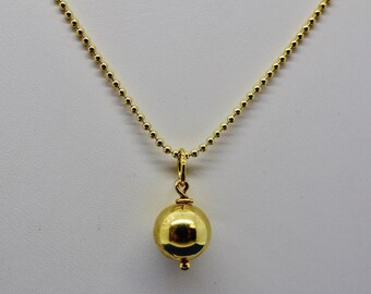 May include: A gold-colored necklace featuring a small, round pendant. The pendant is a shiny sphere suspended from a delicate chain of small, round beads. The necklace is displayed against a plain white background.