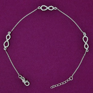 May include: A silver anklet with three infinity symbols, each made of small beads. The anklet has a lobster clasp closure.