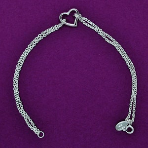 May include: A silver bracelet with a heart-shaped charm. The bracelet has a double chain design and a lobster clasp.