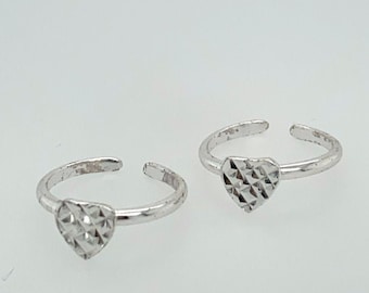 May include: Two silver toe rings with heart-shaped designs. Each ring features a textured heart at the center and an adjustable band. The rings are displayed on a white background.
