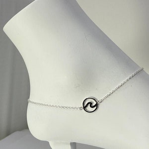 May include: Silver ankle bracelet with a wave design charm. The chain is delicate and the charm is a circle with a wave cut out.