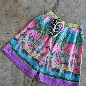 Könnte beinhalten: Eine bunte Badehose mit tropischem Muster, das Palmen, Segelboote und Sonnenschirme zeigt. Die Hose hat einen violetten Bund und einen Kordelzug.