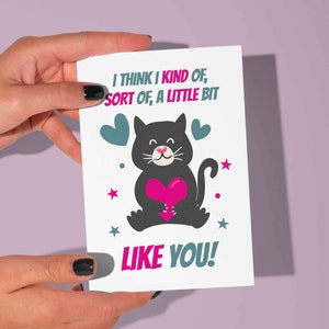 Biglietto d'auguri stampabile di amore e amicizia con citazione "Penso che un po', un po', mi piaci". Biglietto di auguri con un simpatico gatto che tiene in mano un cuore.