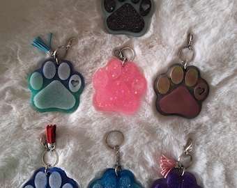 May include: Seven colorful paw print keychains with glitter and a small heart charm. The keychains are made of resin and come in a variety of colors, including blue, green, pink, purple, and brown.