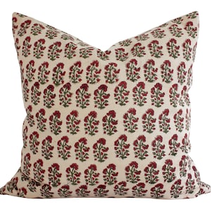May include: A cream-colored pillow with a red and green floral pattern. The pillow is made of a soft, natural fabric and has a subtle sheen.