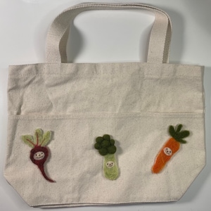 Könnte beinhalten: Eine weiße Stofftasche mit drei Filzapplikationen von Gemüse mit Gesichtern. Das Gemüse sind eine rote Rübe, ein grüner Brokkoli und eine orange Karotte.