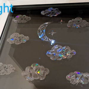 May include: A window with a crescent moon and stars, surrounded by iridescent clouds. The word "Night" is written in blue at the top of the window.