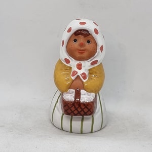 Peut inclure: Une figurine en céramique d'une fille portant une robe à pois blancs et rouges et un bonnet blanc. Elle tient un panier brun dans ses mains.