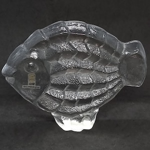 Pode incluir: Uma escultura de vidro transparente de um peixe com uma superfície texturizada. O peixe tem aproximadamente 15 cm de comprimento e 7,5 cm de largura.