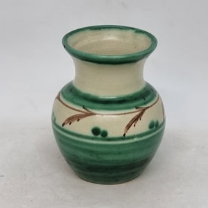 Könnte beinhalten: Eine kleine, grüne und weiße Keramikvase mit braunen Maldetails. Die Vase hat einen runden Körper und einen schmalen Hals.