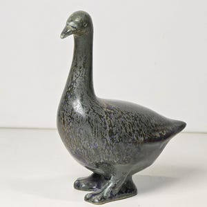 Pode incluir: Estatueta de ganso de cerâmica com um esmalte salpicado cinza escuro e azul. O ganso está em pé com a cabeça erguida, mostrando um pescoço longo e detalhes. A estatueta é um item decorativo.