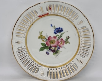 May include: White porcelain plate with a gold rim and a delicate openwork design. The centre features a hand-painted floral motif with pink, yellow, and blue flowers.