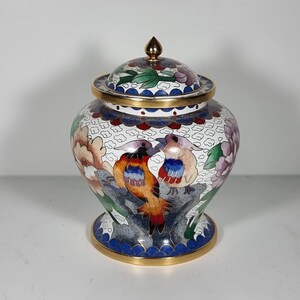 May include: A decorative, lidded jar with a gold finial. The jar features a colorful floral and bird design with red, orange, blue, and purple accents. The base and rim are trimmed with gold and blue.