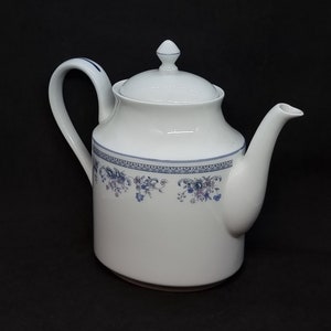 Può includere: Teiera in ceramica bianca con un motivo floreale blu e un coperchio. La teiera ha un manico e un beccuccio.