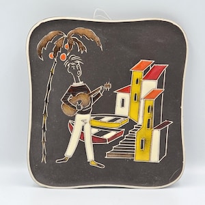 May include: Square ceramic wall hanging with a black background featuring a musician playing a guitar, a palm tree, and colorful buildings. The artwork has a white border and a hanging loop.