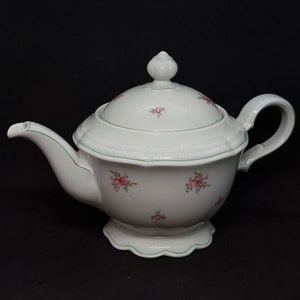 Puede incluir: Tetera de porcelana blanca con ribete verde y estampado floral. La tetera tiene una tapa con un pomo en la parte superior y un asa en el lateral.