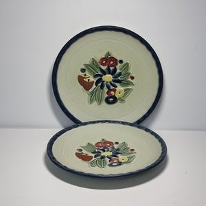 May include: Two white ceramic plates with a blue rim and a raised floral design in shades of red, green, blue, and yellow.