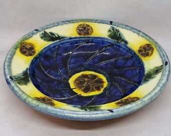 May include: A blue and yellow ceramic bowl with a swirl design and floral accents. The bowl has a white rim and is decorated with yellow and green accents.