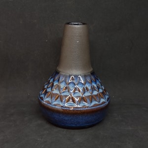 Könnte beinhalten: Eine dunkelbraune und blaue Keramikvase mit geometrischem Muster. Die Vase hat einen breiten Boden und einen schmalen Hals.