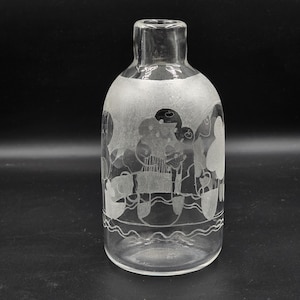 Pode incluir: Garrafa de vidro transparente com design gravado. O design apresenta figuras e formas, com uma linha ondulada perto da base. A garrafa tem um corpo arredondado e um gargalo estreito. O fundo é preto.