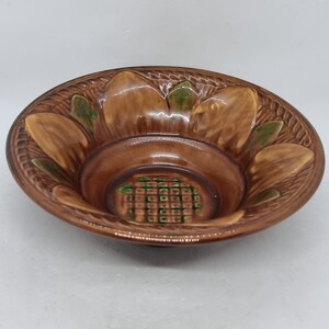 May include: A brown ceramic bowl with a green and brown floral design. The bowl has a raised rim and a slightly indented center.