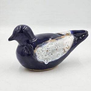 May include: A ceramic bird ornament with a glossy navy blue finish. The bird features a speckled white and tan pattern on its back and wings. It has a small, pointed beak. This is a decorative item.