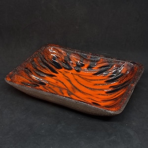 May include: A square ceramic dish with a wavy, abstract design in shades of orange and black.