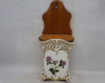 May include: White ceramic wall mounted spice rack with a wooden lid. The rack features a gold trim and a floral design with purple clover flowers. The rack is labeled "GP".