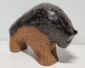 May include: A ceramic sculpture of a brown and black bison. The bison is standing on all four legs and has its head lowered. The sculpture is made of a rough, textured clay.