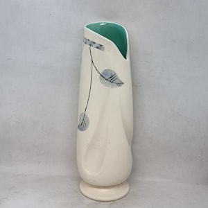 Puede incluir: Un jarrón de cerámica blanco con un borde verde y un diseño de hojas estilizado en azul y negro.
