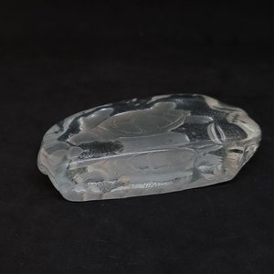 May include: A clear glass ashtray featuring a turtle design. The ashtray is rectangular with rounded edges and a shallow bowl. The turtle is etched into the glass, set against a black background.