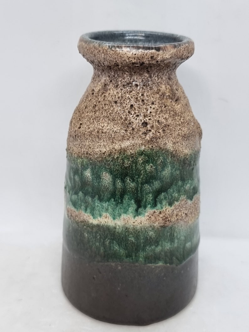 Puede incluir: Un jarr&oacute;n peque&ntilde;o de cer&aacute;mica marr&oacute;n y verde con una superficie texturizada. El jarr&oacute;n tiene una base ancha y un cuello estrecho.