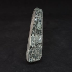 May include: A clear, rectangular glass object with a textured surface. The glass has a slightly curved shape and appears transparent with internal swirls. The object is set against a black background.