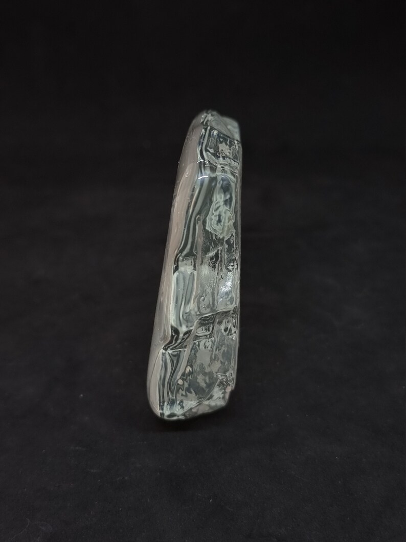 May include: A clear, rectangular glass object with a textured surface. The glass has a slightly curved shape and appears transparent with internal swirls. The object is set against a black background.