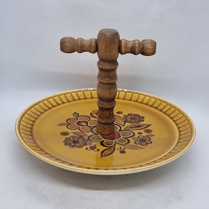 Könnte beinhalten: Ein gelbes Keramik-Serviertablett mit Blumenmuster und einem Holzgriff. Das Tablett hat einen erhöhten Rand und eine glatte Oberfläche.