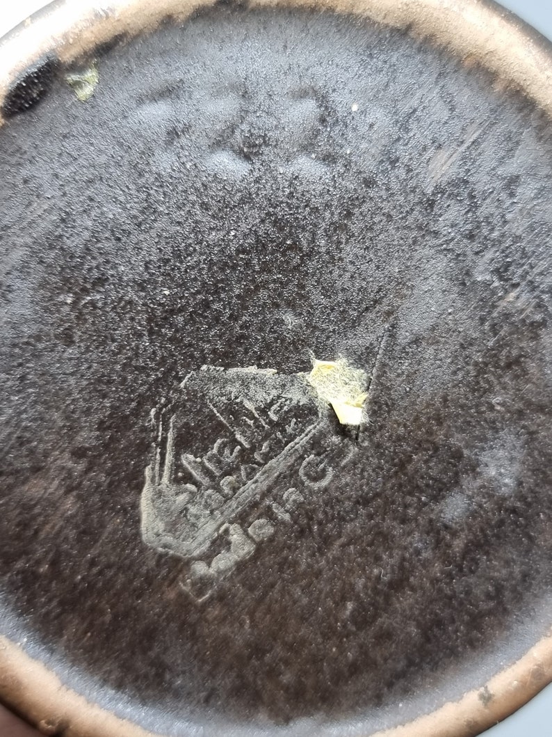 Puede incluir: Primer plano de la parte inferior de una olla de cer&aacute;mica marr&oacute;n con una marca dorada que dice "Wilhelm  Wacker  Barmen".