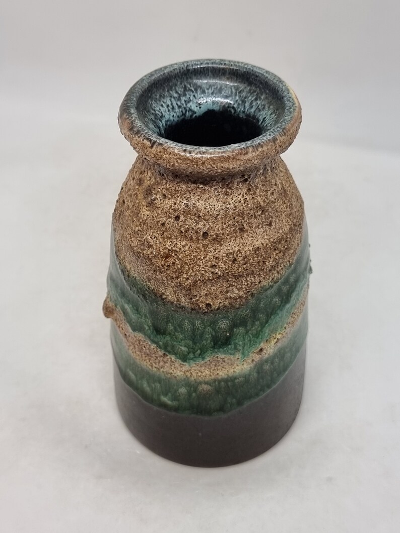 Puede incluir: Un peque&ntilde;o jarr&oacute;n de cer&aacute;mica marr&oacute;n con un esmalte verde y azul. El jarr&oacute;n tiene una superficie texturizada y una boca ancha.