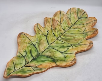 May include: A ceramic leaf-shaped dish with a green and orange glaze. The dish is hand-painted with details of veins and a textured surface.