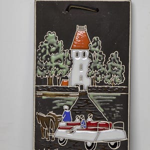 Puede incluir: Una placa de pared de cerámica con fondo negro y un edificio blanco con techo naranja. El edificio está rodeado de árboles verdes y un bote rojo con personas en él. El bote está siendo tirado por un caballo marrón.