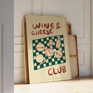 Könnte beinhalten: Ein gerahmtes Poster mit den Worten "Wine & Cheese Club" in roter Schrift. Das Poster zeigt ein grün-weiß kariertes Tischtuchdesign mit Illustrationen von Wein, Käse, Tellern und Besteck. Das Poster lehnt an einer Wand.