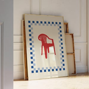 Könnte beinhalten: Gerahmter Kunstdruck mit einer roten Stuhldarstellung auf cremefarbenem Hintergrund. Das Kunstwerk ist von einem blau-hellblauen Schachbrettmuster umrandet. Der Rahmen hat einen goldenen Rand. Der Druck lehnt an einer Wand.