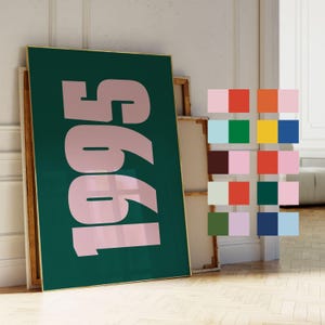 May include: A framed art print featuring the number "1995" in a pale pink font against a dark green backdrop. A colour palette of various squares is to the right. The frame has a gold border.
