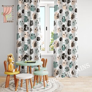May include: Two white curtains with a pattern of black, teal, and peach fish. The curtains are hung in a room with a window and a small table with three chairs.