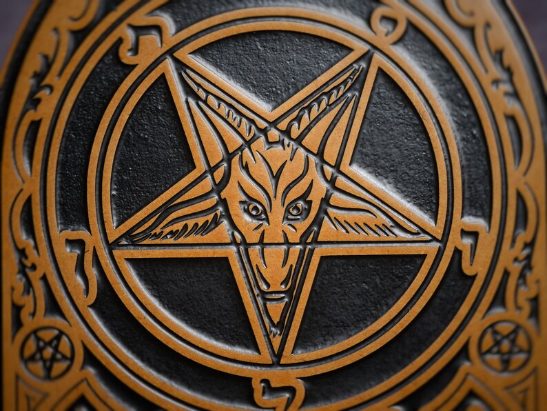 May include: A black and gold pentagram with a goat's head in the centre. The pentagram is surrounded by a circle with decorative designs.